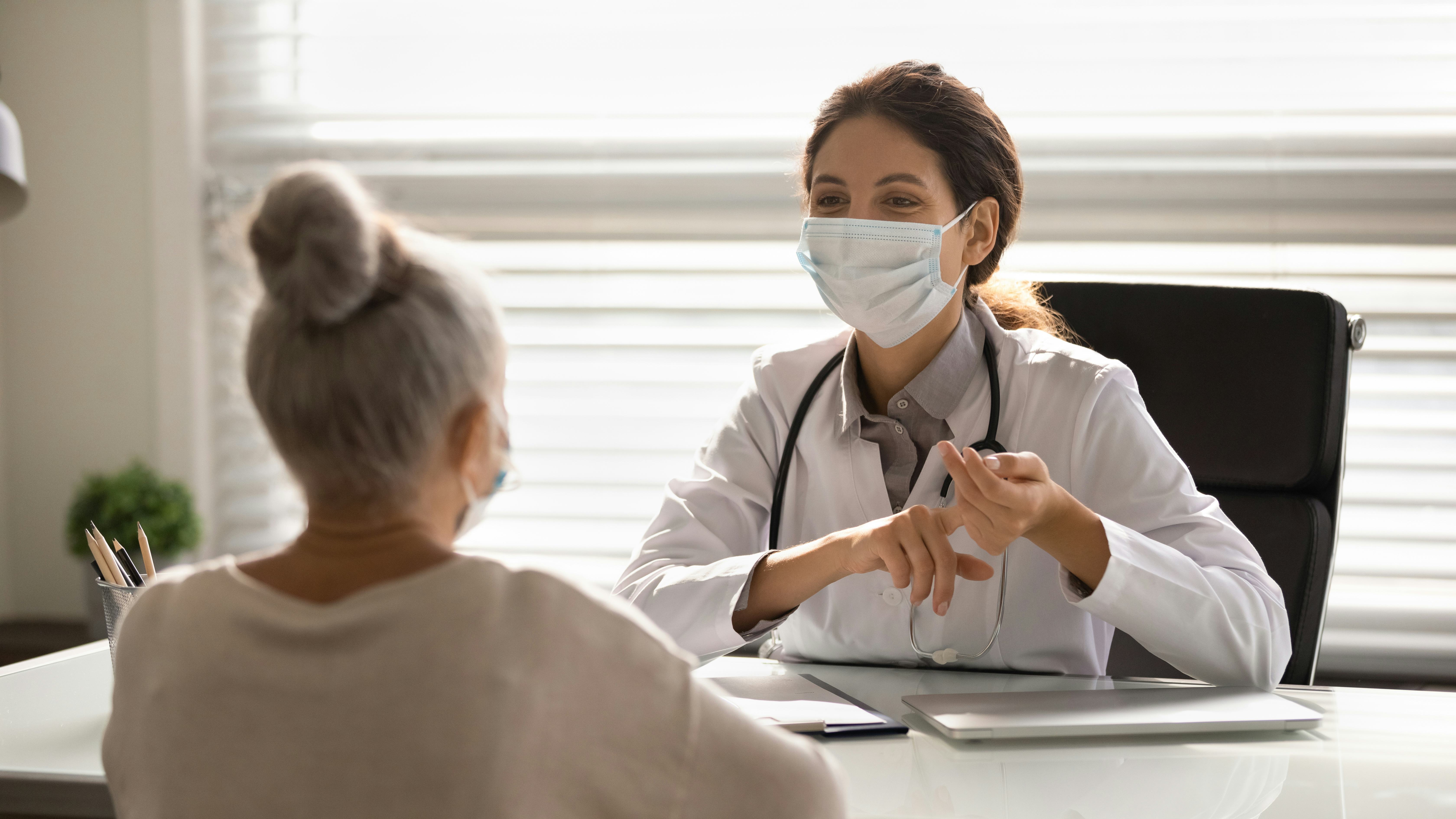 Female doctor in medical facial mask have consultation with elderly patient during covid-19 pandemic...