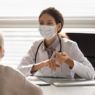 Female doctor in medical facial mask have consultation with elderly patient during covid-19 pandemic...