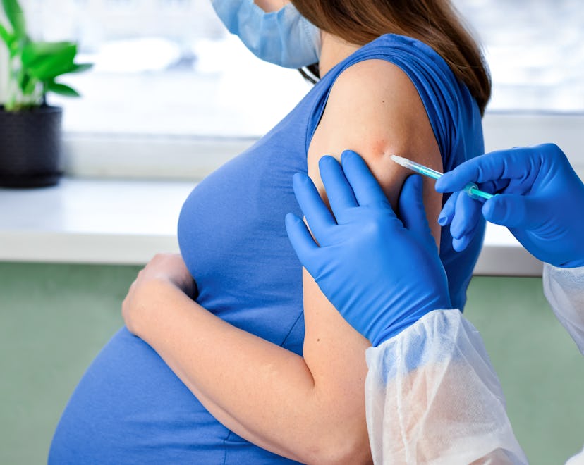 Image of a pregnant adult, wearing a protective face mask, receiving a needle shot in the upper arm....