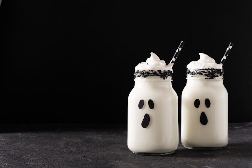 Funny white milkshake ghost cocktail on black background, halloween concept, copy space