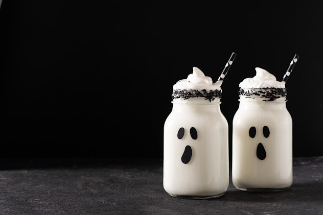 Funny white milkshake ghost cocktail on black background, halloween concept, copy space