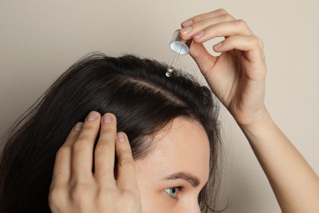 Woman applying oil onto hair on grey background, closeup. Baldness problem