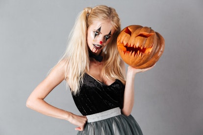 Woman in clown halloween makeup posing with carved pumpkin