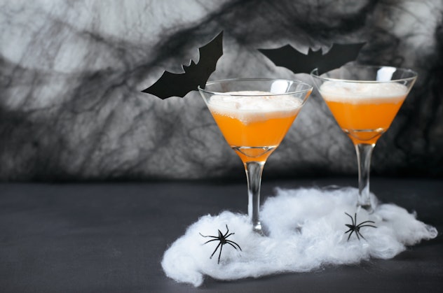 Halloween pumpkin cocktail food concept, glasses with spider web, black bats and spiders on dark background ...