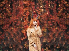 woman with deer makeup and horns in autumn forest during halloween