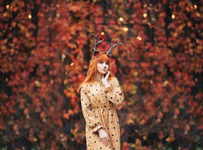 woman with deer makeup and horns in autumn forest during halloween