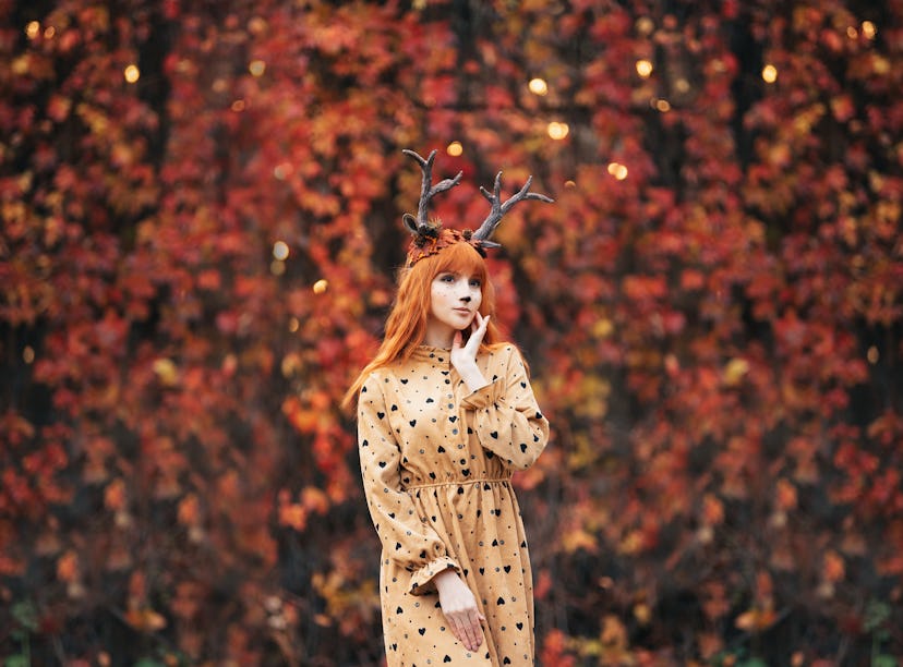 woman with deer makeup and horns in autumn forest during halloween