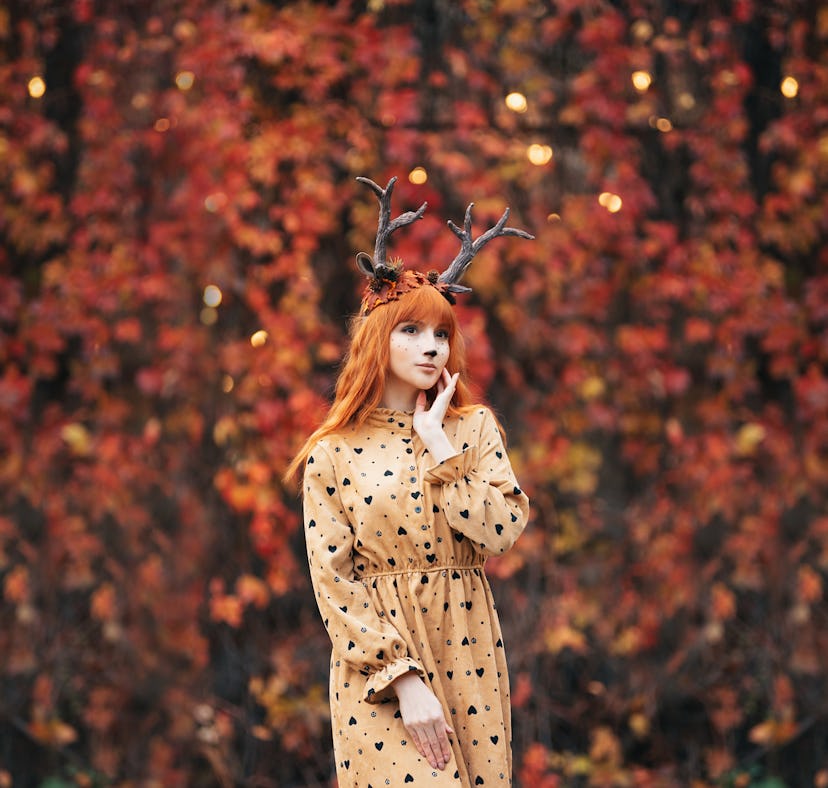 woman with deer makeup and horns in autumn forest during halloween