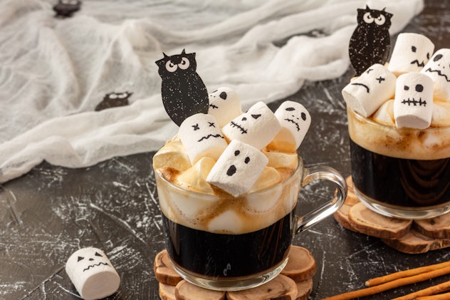 Two cups coffee with marshmallow (spooky faces, monster, bats) for Halloween on dark background. Cop...
