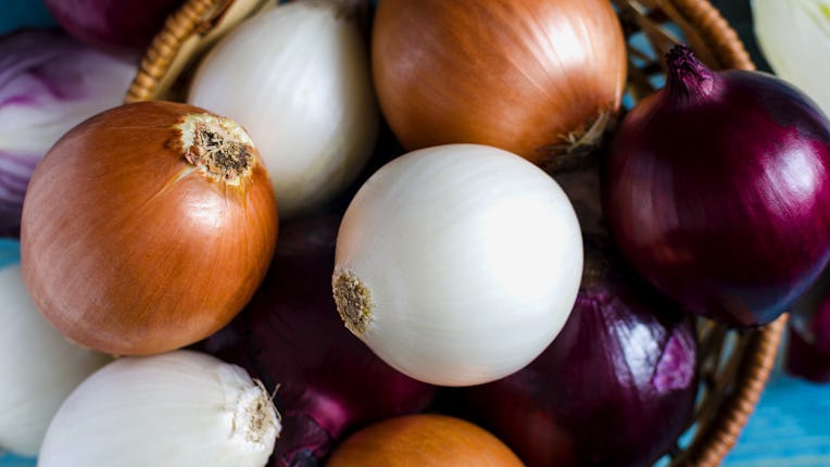 large bulbs of yellow, red and white onions close-up in a wicker basket