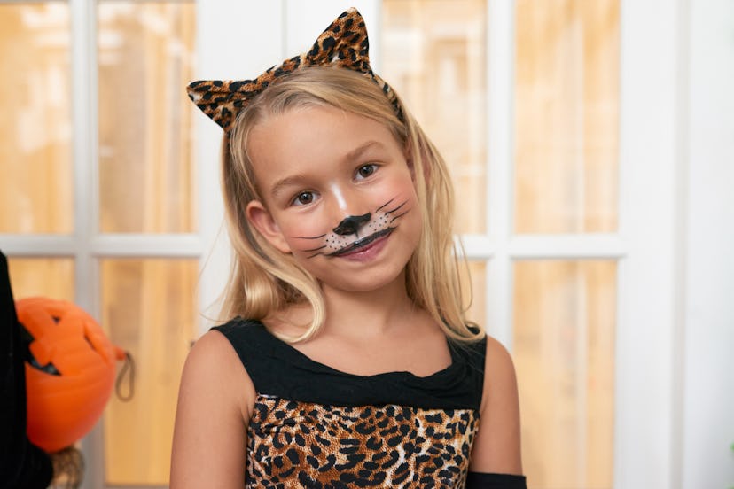 Portrait of little beautiful blond Caucasian girl in leopard dress with headband and face painting s...