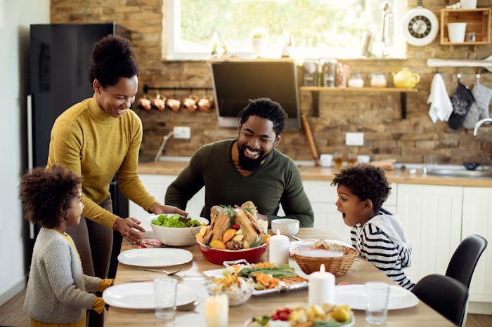 Happy African American parents and their kids having Thanksgiving lunch at home.