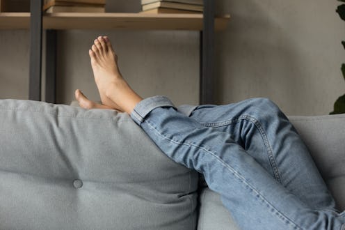 Crop close up of woman lying relaxing on comfortable grey couch in living room on lazy domestic week...