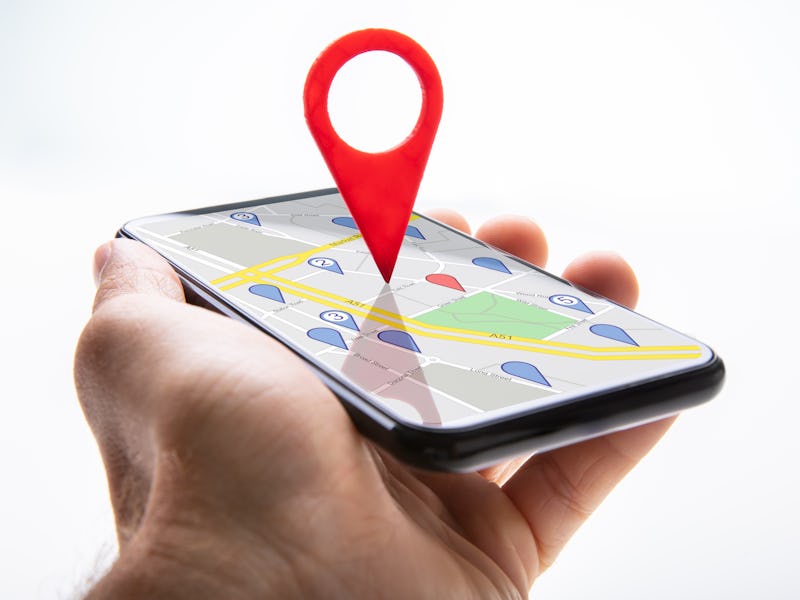 Close-up Of A Person's Hand Holding Cellphone With Red Map Pin Pointer Against White Background