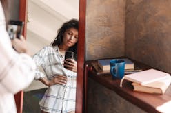 Photo of attractive brunette woman wearing shirt taking selfie photo and looking at mirror in apartm...