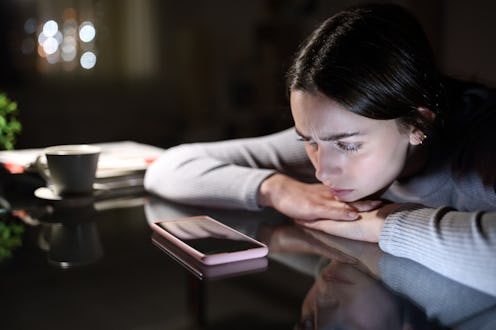 Sad woman waiting for a mobile phone call looking it in the night at home