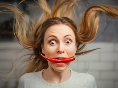 A girl with a red hot pepper in her teeth. Chili for cooking. The spicy seasoning is very stinging i...