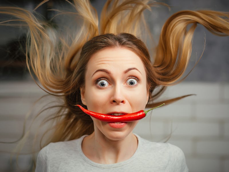 A girl with a red hot pepper in her teeth. Chili for cooking. The spicy seasoning is very stinging i...