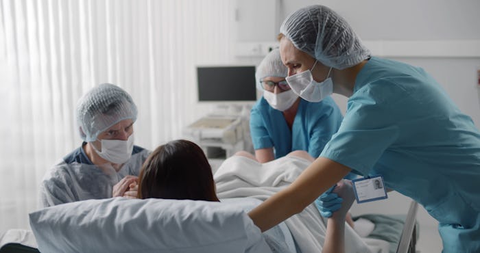 Woman giving birth with husband holds her hand in support and obstetricians assisting. Back view of ...