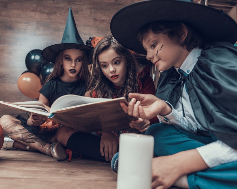 Little Children in Halloween Costumes Reading Book. Cute Smiling Kids wearing Scary Halloween Costum...