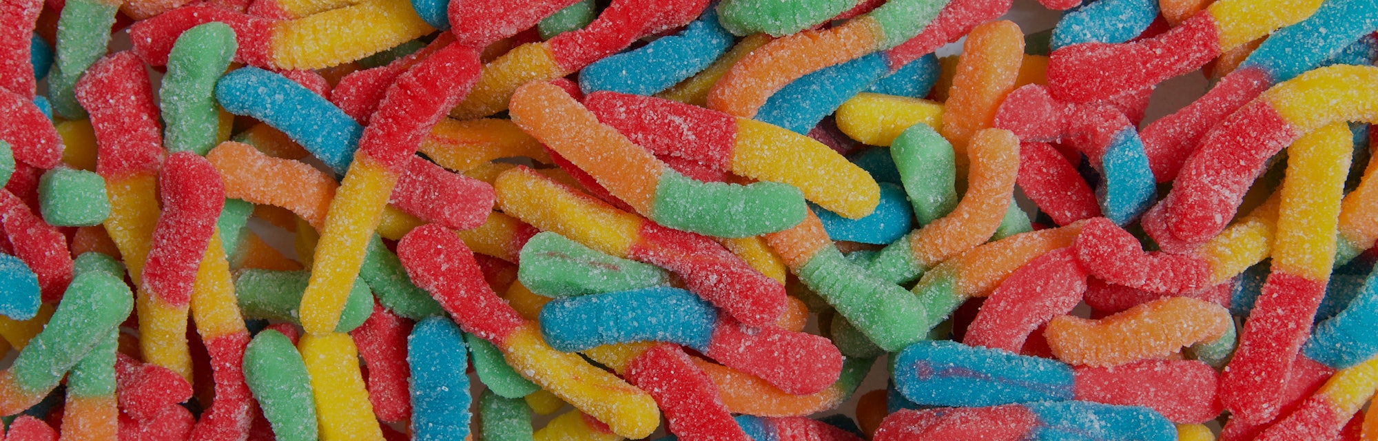 Sour candy gummy worms close up background. Covered in granulated sugar. Flat lay top view from abov...