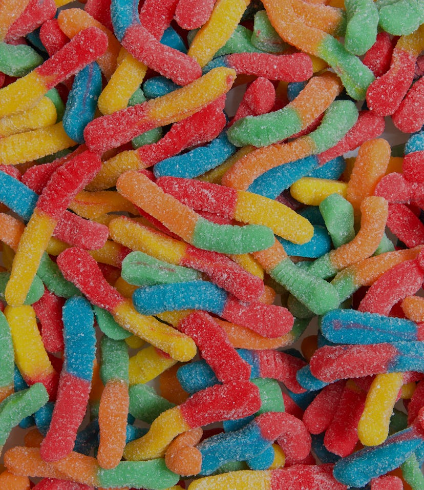 Sour candy gummy worms close up background. Covered in granulated sugar. Flat lay top view from abov...