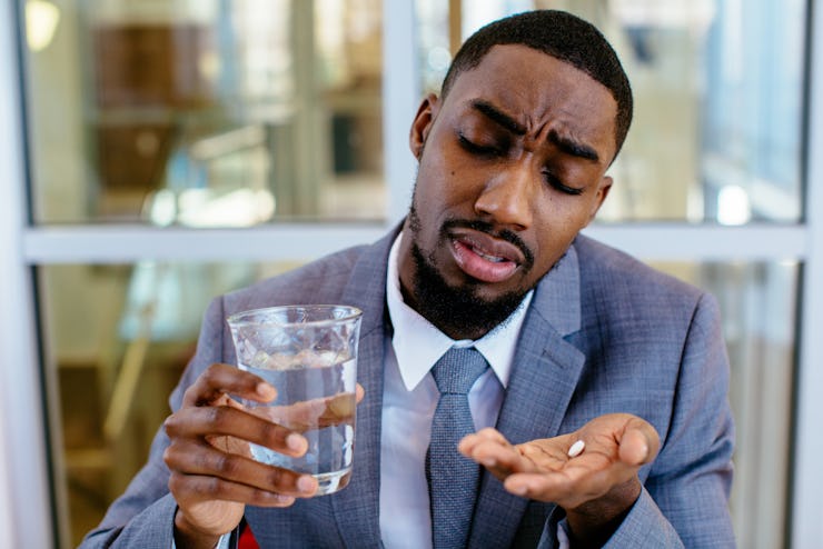 Portrait of a sick young man in business suit taking a medicine pill with water