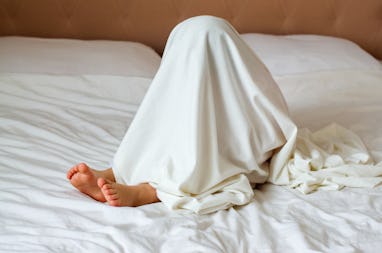 Little child hiding under white blanket in bedroom. Play therapy at home. Toddler child playful, pla...
