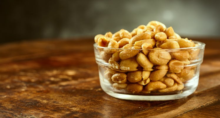 Glass bowl of fresh roasted salted peanuts or groundnuts on an old wooden table or bar counter in a ...