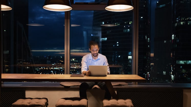 Full length African American businessman working on laptop in office at night alone, looking at scre...