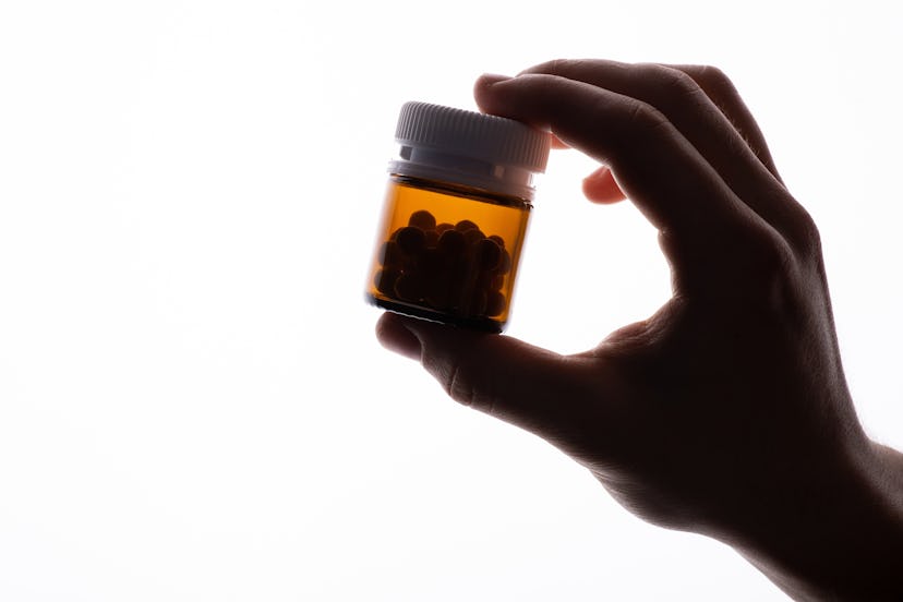 Black shape of human's hand, medical bottle with pills, close up, isolated. Copy space on the left s...