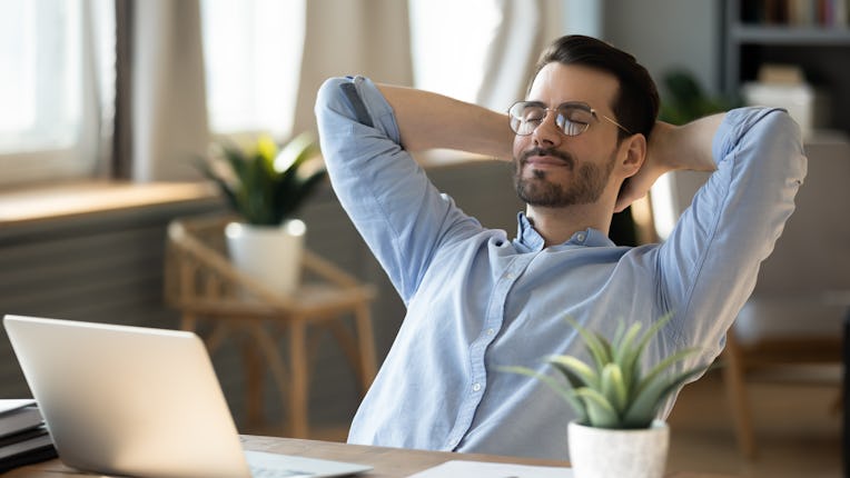Calm millennial man in glasses sit relax at home office workplace take nap or daydream. Happy relaxe...