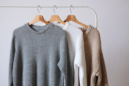 Warm sweaters on a wardrobe hanger on a light background. Autumn, winter clothes.