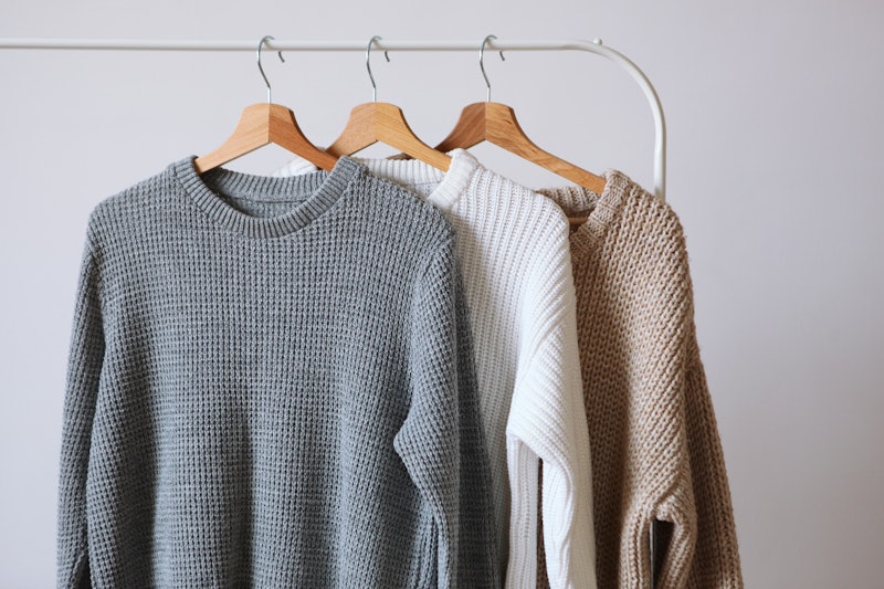 Warm sweaters on a wardrobe hanger on a light background. Autumn, winter clothes.
