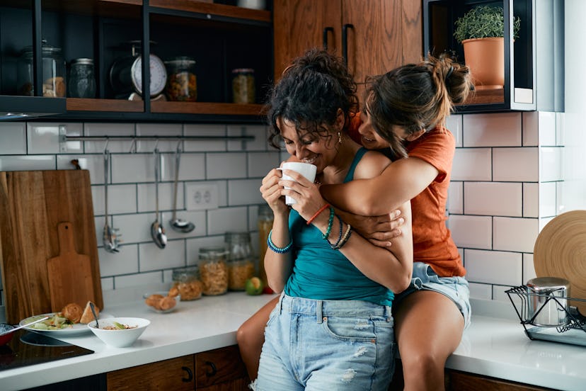Young happy lesbian women drinking coffee and having fun in the kitchen.