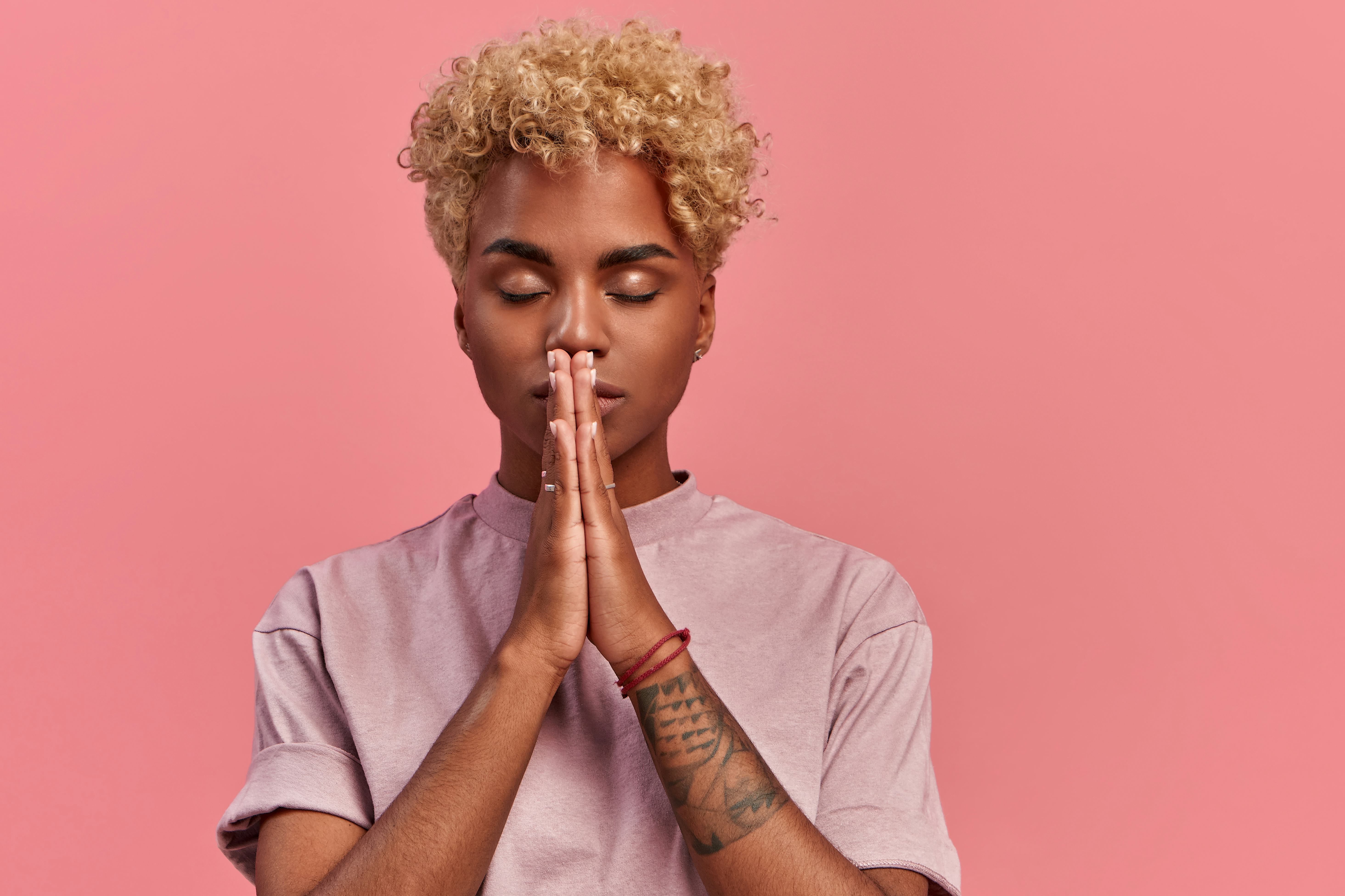 Grateful hopeful young black woman stands in meditative pose, enjoys peaceful atmosphere, holds hand...
