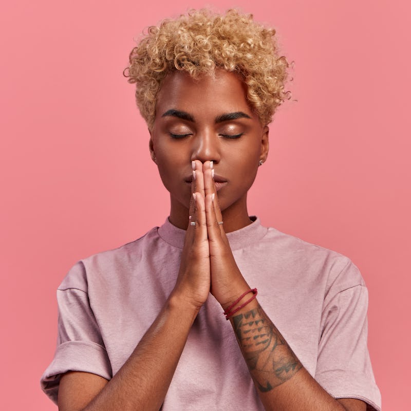 Grateful hopeful young black woman stands in meditative pose, enjoys peaceful atmosphere, holds hand...