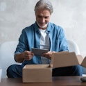Smiling man consumer open cardboard box get postal parcel, male customer receive carton package sit ...