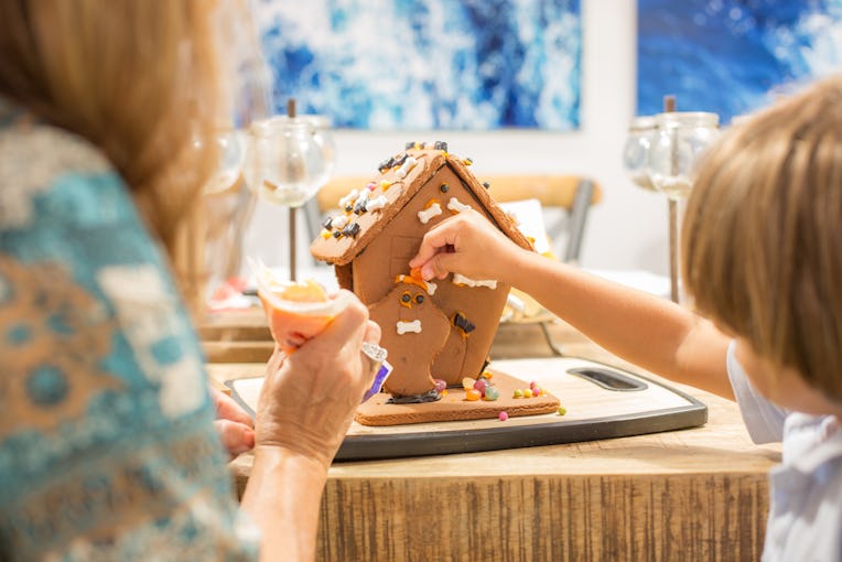 Boy decorating Halloween gingerbread house in the fall month of October using sweet candy ghost and ...