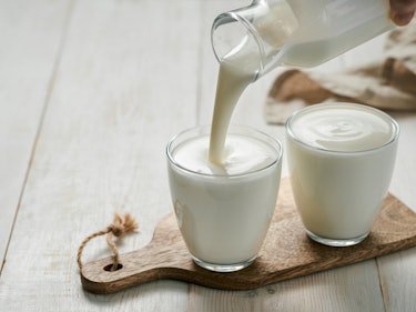 Pouring homemade kefir, buttermilk or yogurt with probiotics. Yogurt flowing from glass bottle on wh...