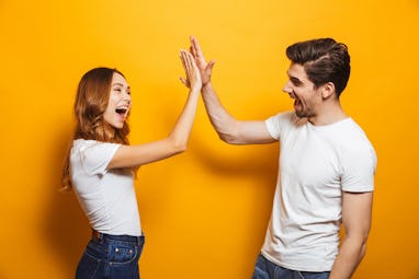 Image of friendly young people man and woman in basic clothing laughing and giving high five isolate...