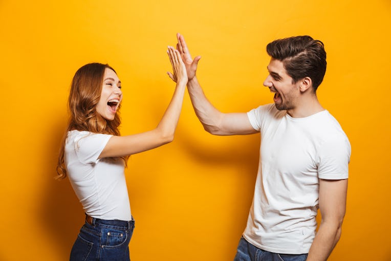 Image of friendly young people man and woman in basic clothing laughing and giving high five isolate...