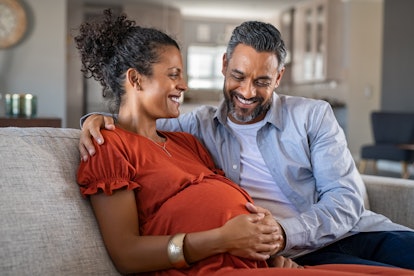 happy couple sitting with husband's hand on wife's pregnant stomach in an article about not gaining ...