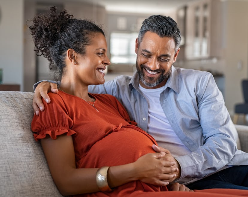 Mid adult couple expecting a baby while husband caresses the belly of his pregnant african woman. Lo...