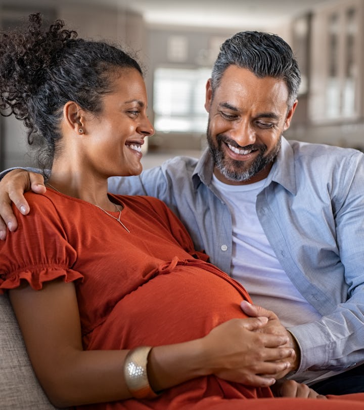 Mid adult couple expecting a baby while husband caresses the belly of his pregnant african woman. Lo...