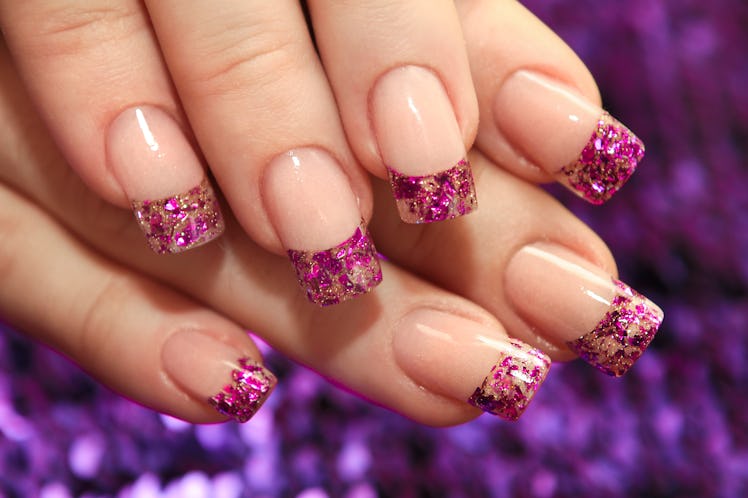 Brilliant French manicure with lilac and golden small glitters on a purple background close-up. 