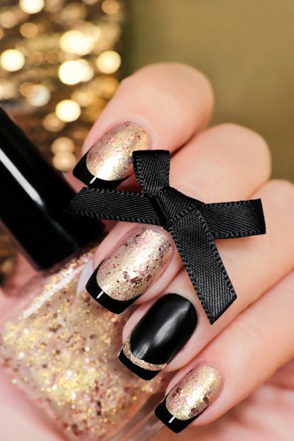 Black and gold, glittery French manicure with nail Polish in hand closeup.