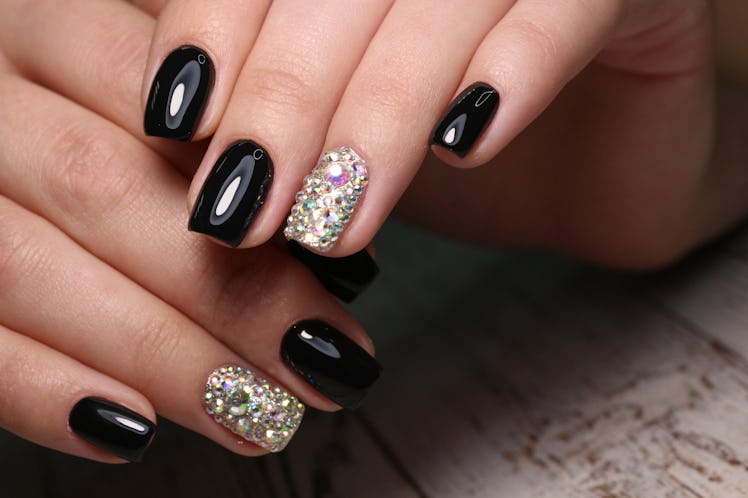 A gel, black manicure with rhinestones on the ring finger.