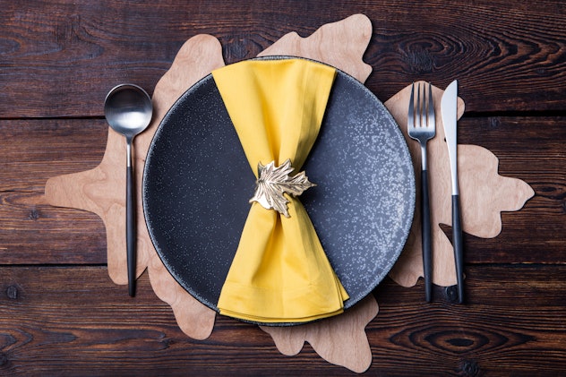 Close-up image of an autumnal place setting on a table, with yellow napkin displayed on a circular b...