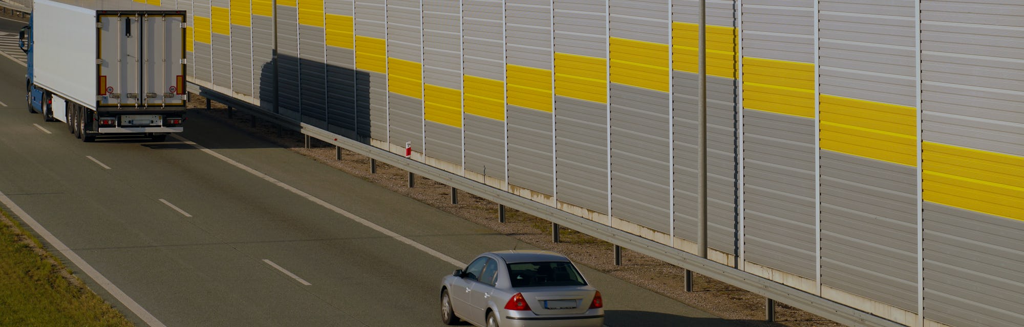 Road transport. Truck and passenger car moving along the highway protected by sound barriers.